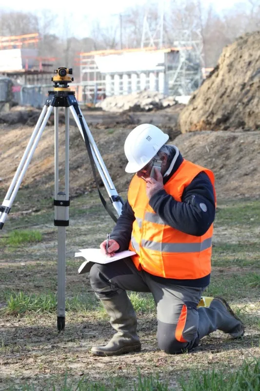 Surveyor kneeling on phone next to theodolite