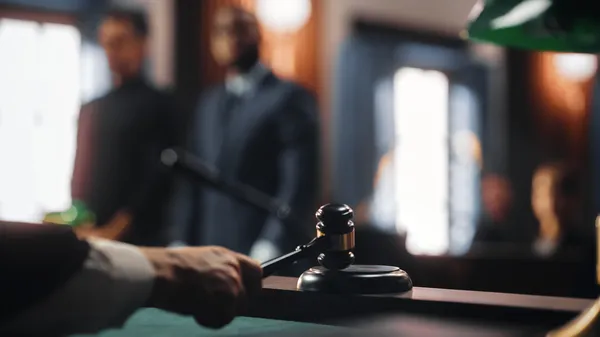 Photo of a judge banding a gavel in front of a courtroom with blurred defendants in the background