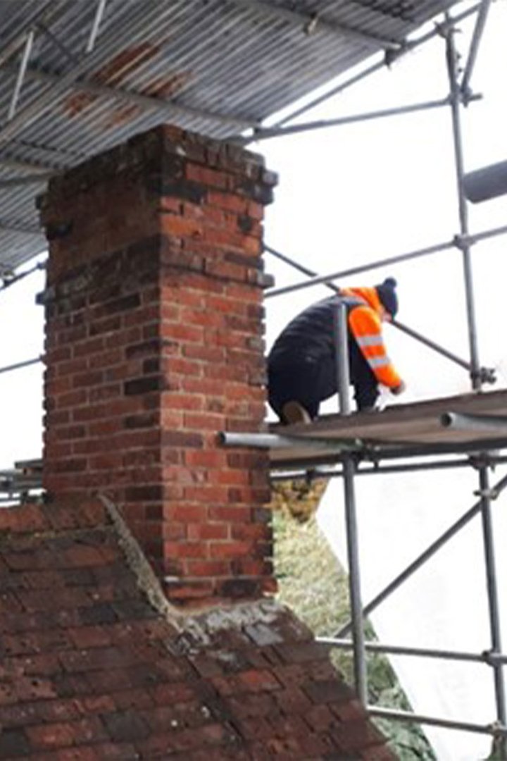 Photo showing the removal of a chimney stack with a construction worker on scaffolding